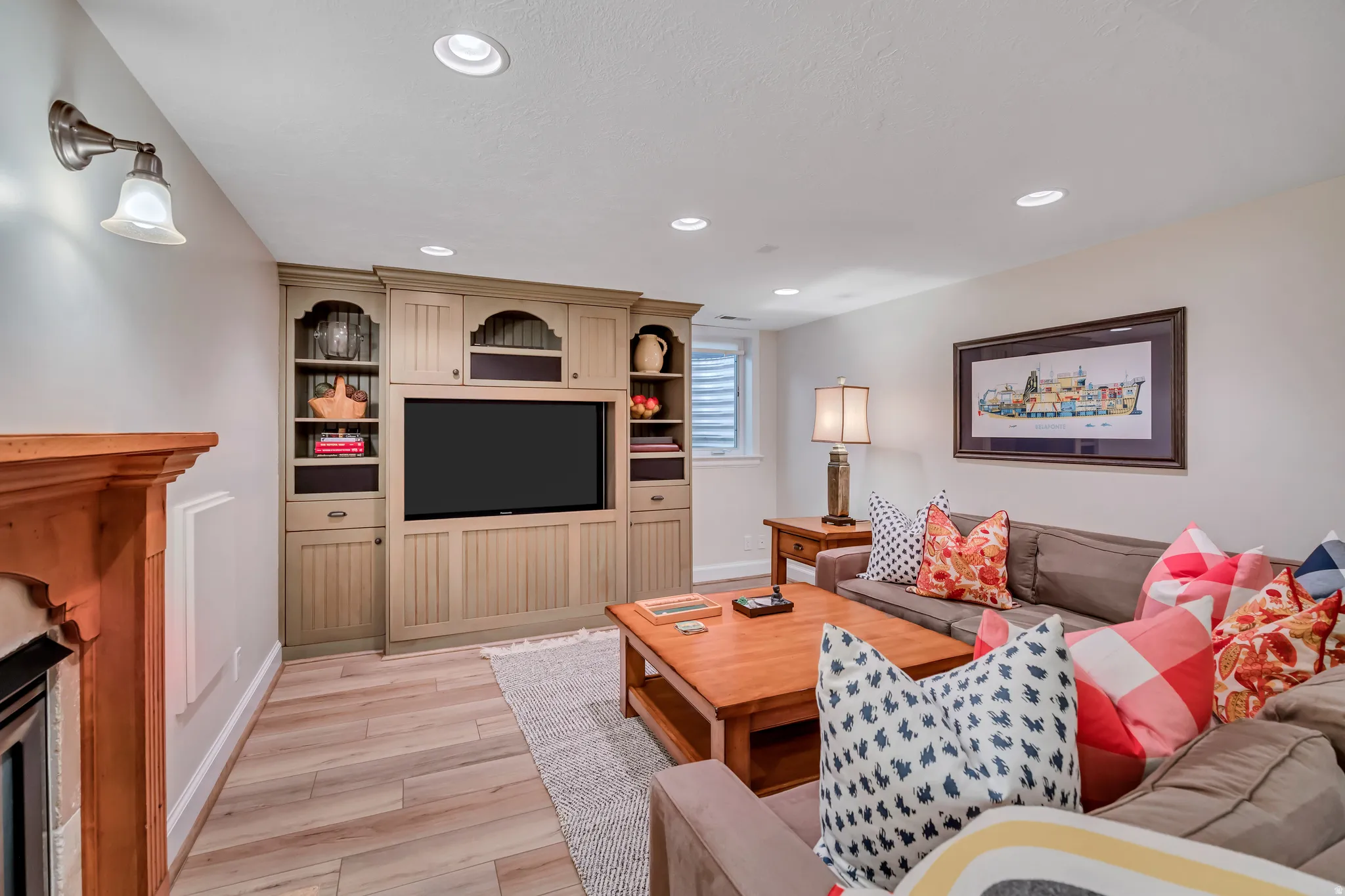 Entertainment space featuring custom built-in cabinetry, recessed lighting, wood-finish flooring, and a fireplace with a wood mantel