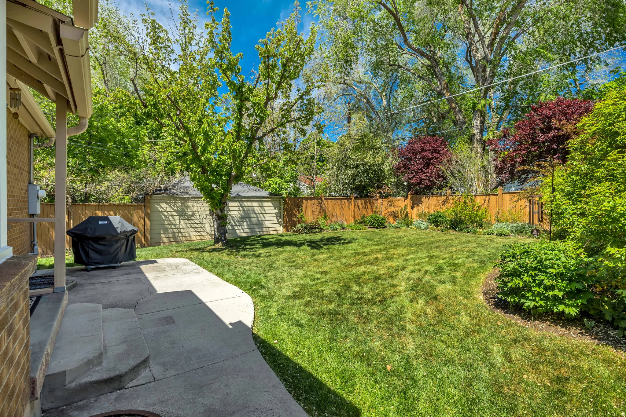 Expansive backyard featuring a manicured lawn, established perimeter landscaping, and mature trees