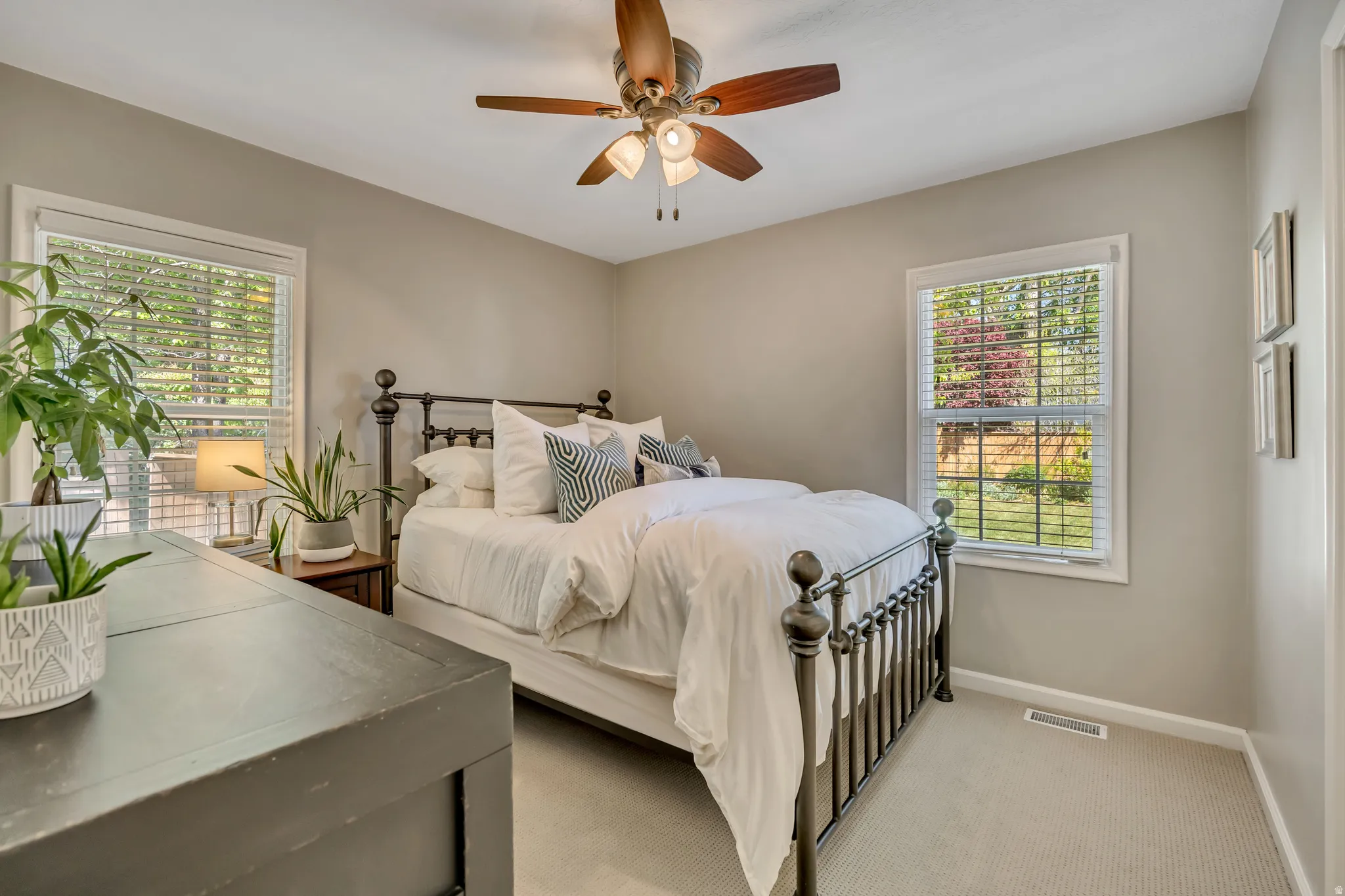Bedroom featuring two windows with white blinds, a ceiling fan with light fixture, light gray wall paint, and gray carpeting