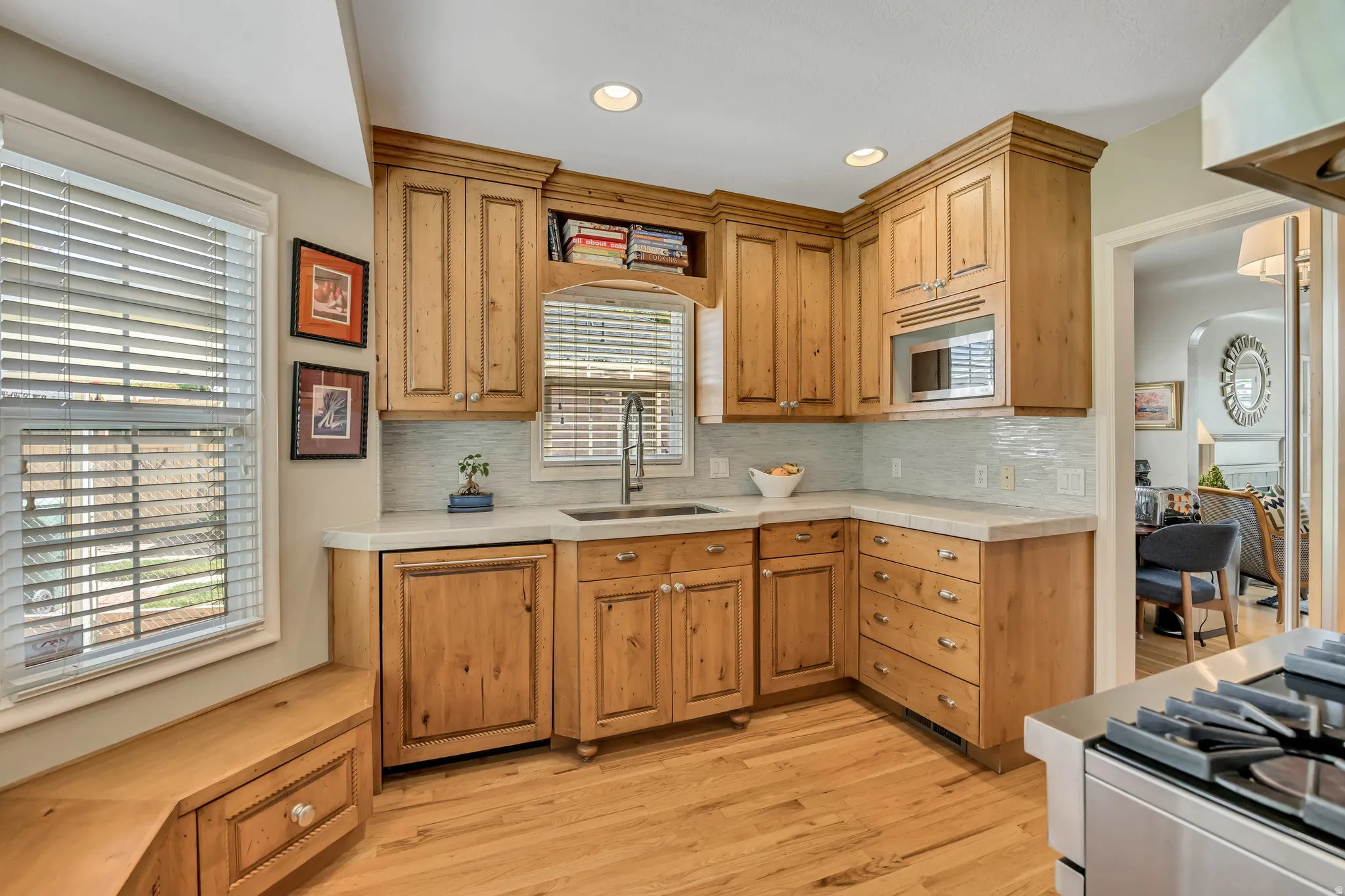Kitchen featuring wood cabinetry, light-toned countertops, a tile backsplash, stainless steel sink, and wood-finish flooring
