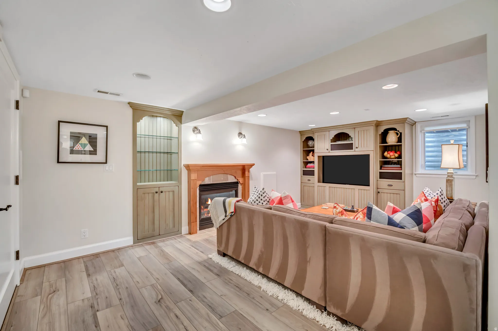 Spacious entertainment area featuring wood-finish flooring, a built-in media center with shelving, a fireplace with wood mantel, recessed lighting, and a built-in display cabinet