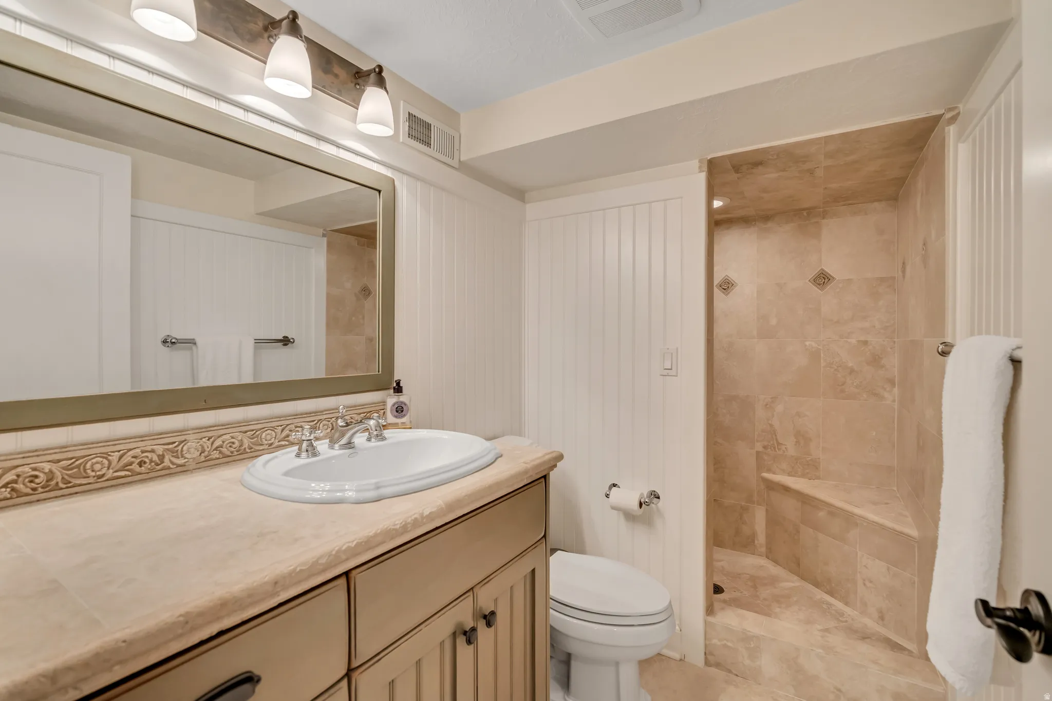 Bathroom featuring a neutral palette, a built-in vanity with an undermount sink and a stone countertop, a large framed mirror, and a walk-in shower with a built-in bench and tiled walls