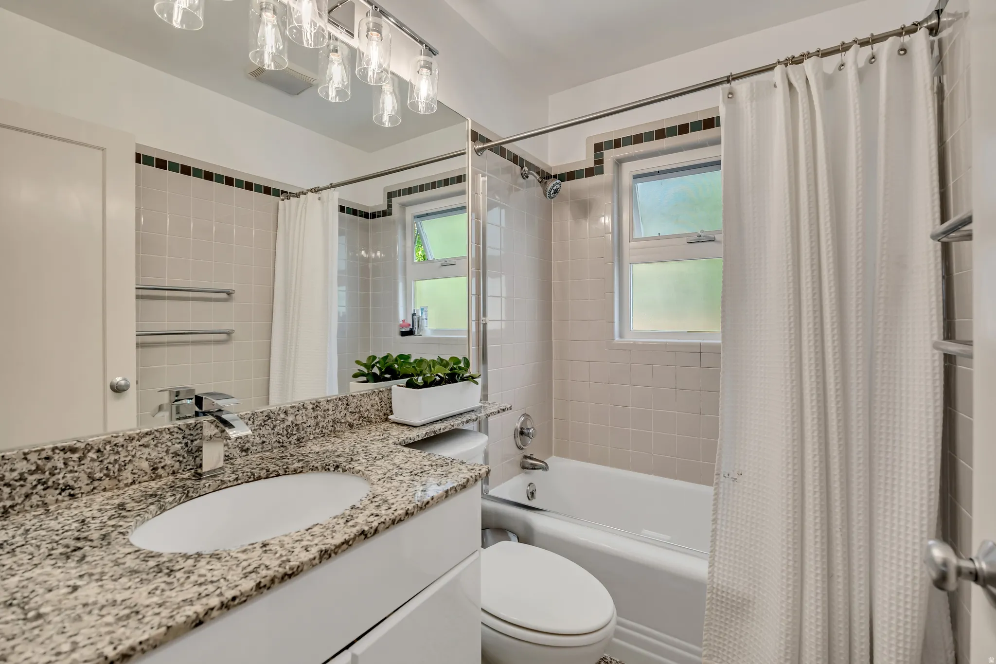 Bathroom featuring a granite countertop vanity with an undermount sink, a chrome faucet, a tub-shower combination with tiled walls, and a window providing natural illumination