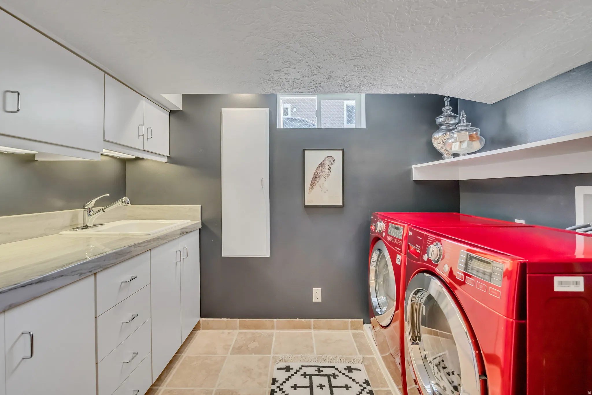 Laundry area featuring white cabinetry, a utility sink with a chrome faucet, light-toned countertop, and tiled flooring