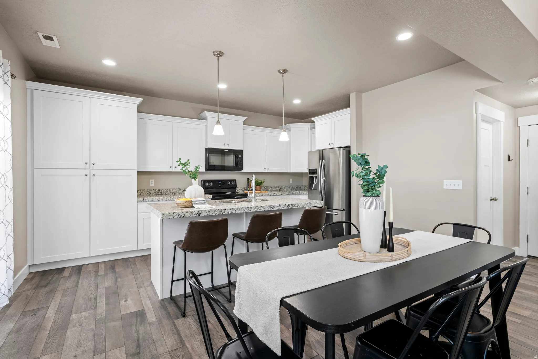 Open-concept kitchen and dining area featuring wood-finish flooring, white cabinetry, a kitchen island with seating, a stainless steel refrigerator, and recessed lighting
