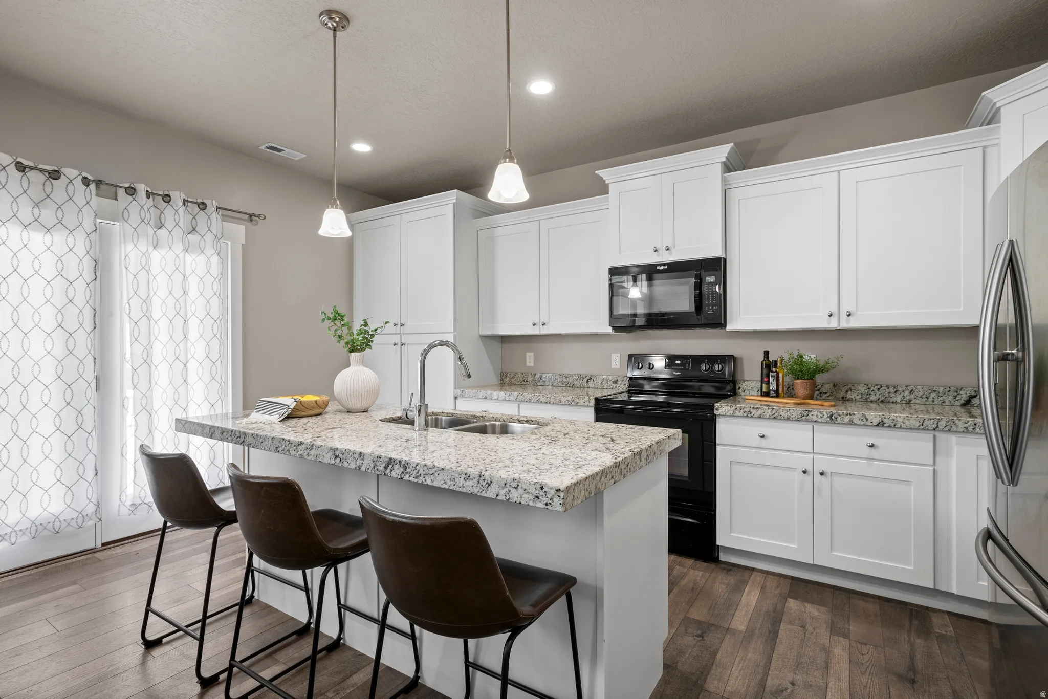 Kitchen featuring white cabinetry, granite countertops, stainless steel appliances, wood-finish flooring, and pendant lighting over a breakfast bar