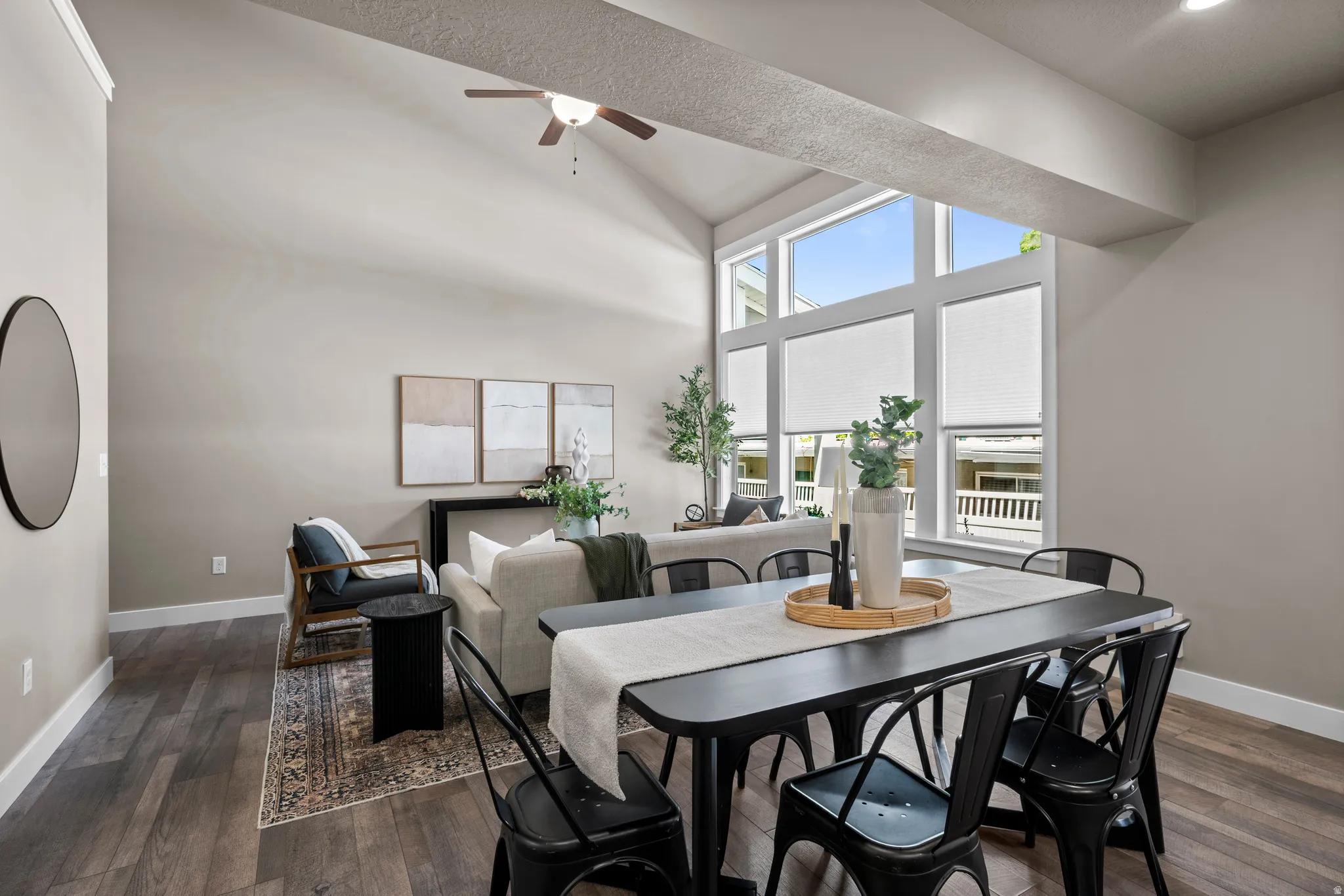 Great room featuring vaulted ceilings, wood-finish flooring, a contemporary ceiling fan, and large windows with privacy blinds