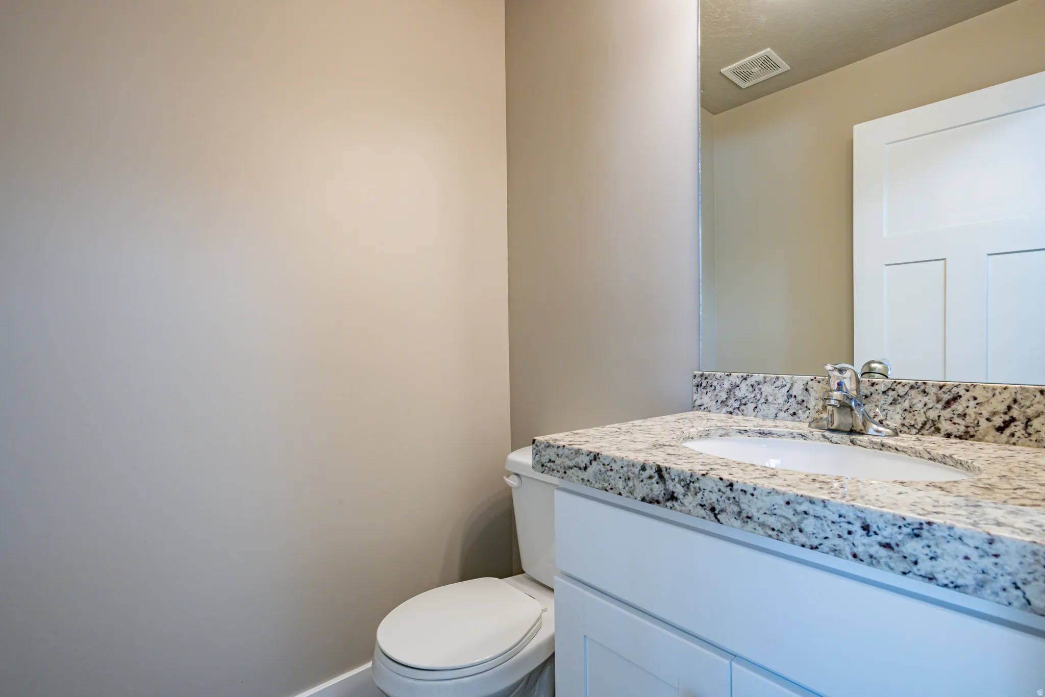 Bathroom vanity featuring a speckled countertop, undermount sink, and chrome faucet