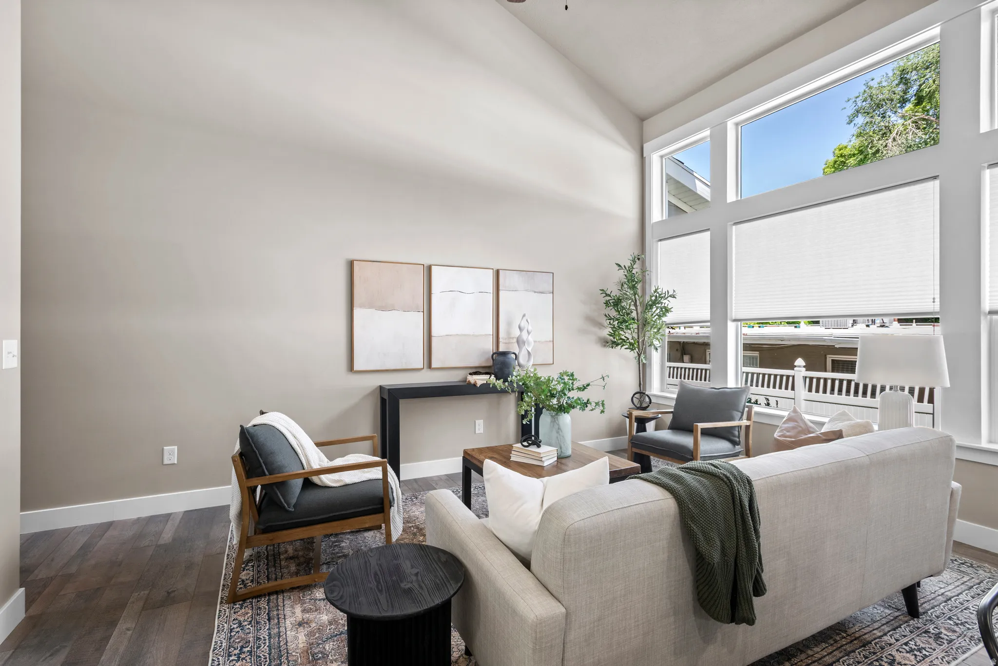 Living area featuring vaulted ceilings, floor-to-ceiling windows with roller shades, wood-finish flooring, and neutral wall tones