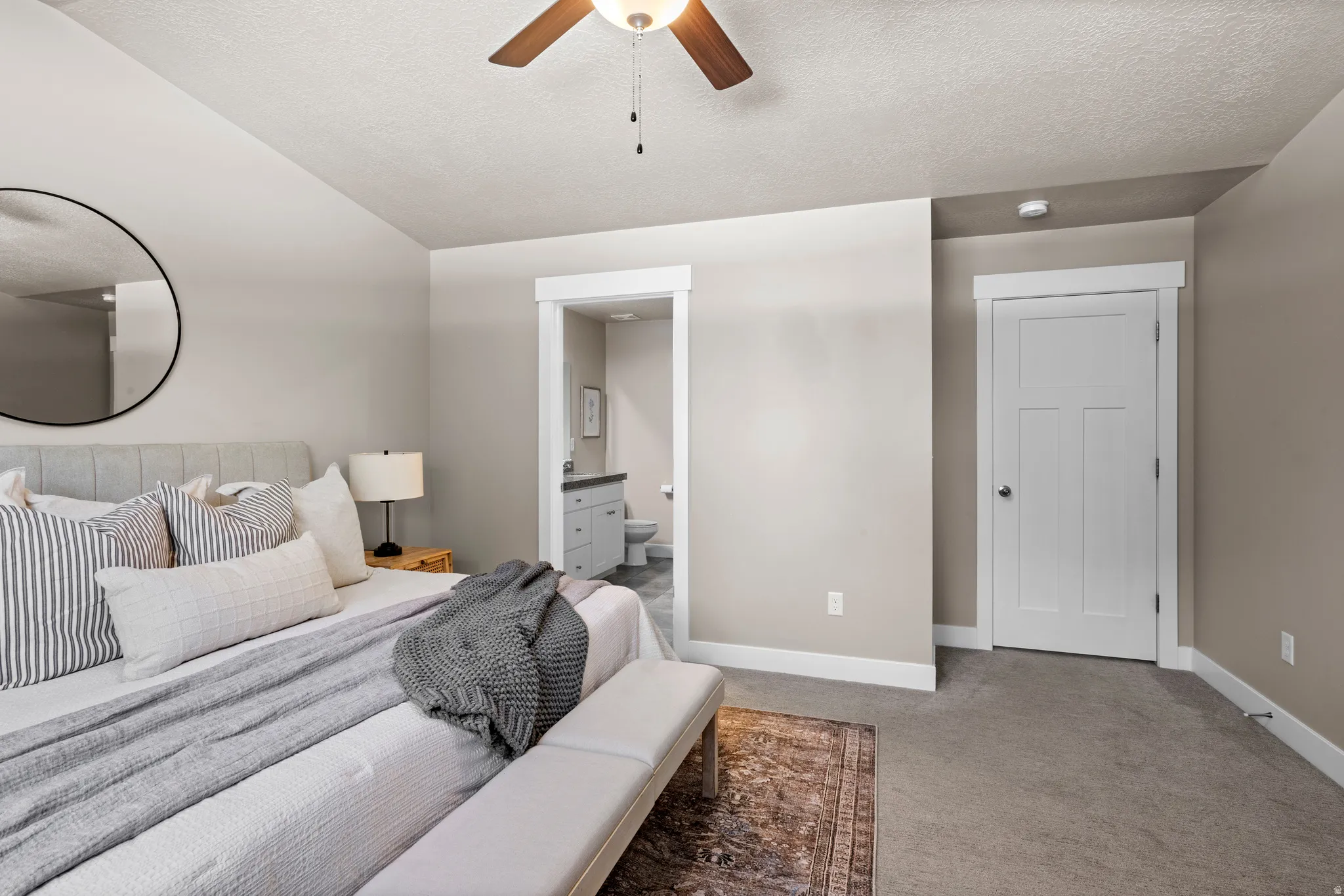 Carpeted bedroom featuring a ceiling fan, a contemporary white interior door, and a private bath with a single vanity and toilet