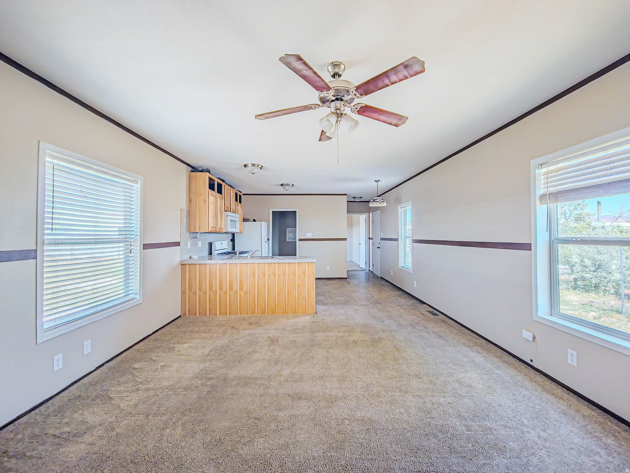 Open-concept living space featuring neutral carpet flooring, a ceiling fan with integrated lighting, and multiple windows with blinds