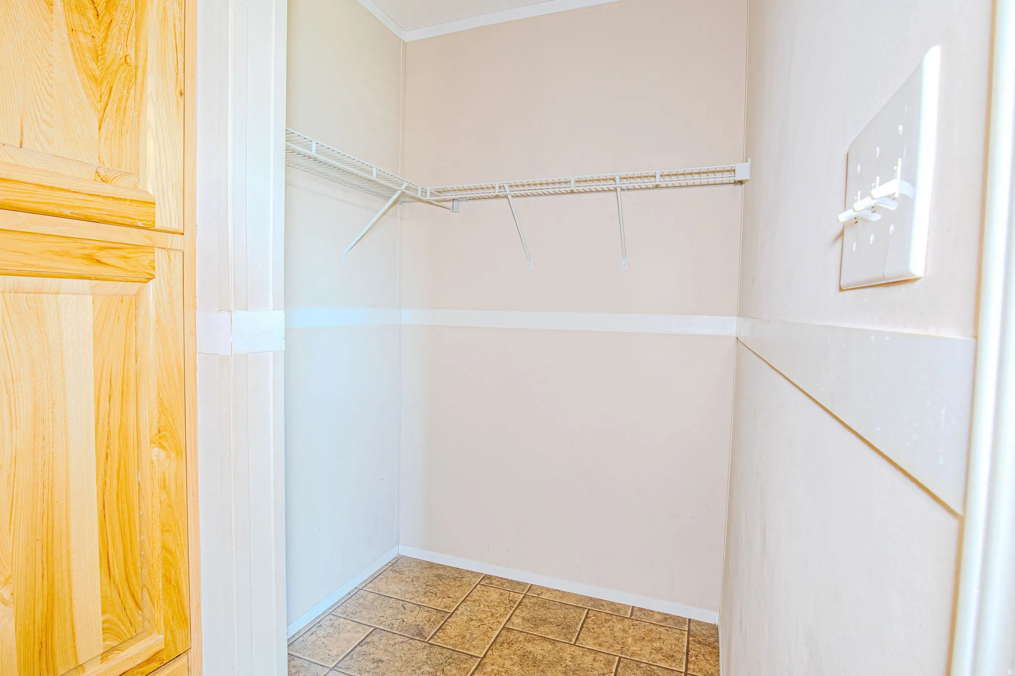 Storage closet featuring wire shelving, neutral wall tones, chair rail detailing, and tiled flooring