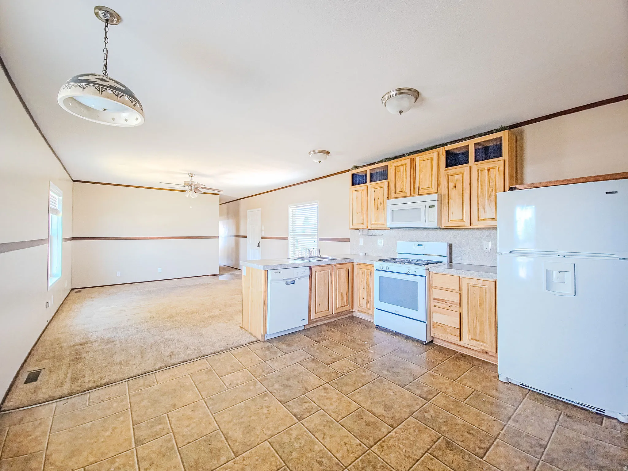 Open-concept kitchen featuring light wood cabinetry, white appliances, and tiled flooring