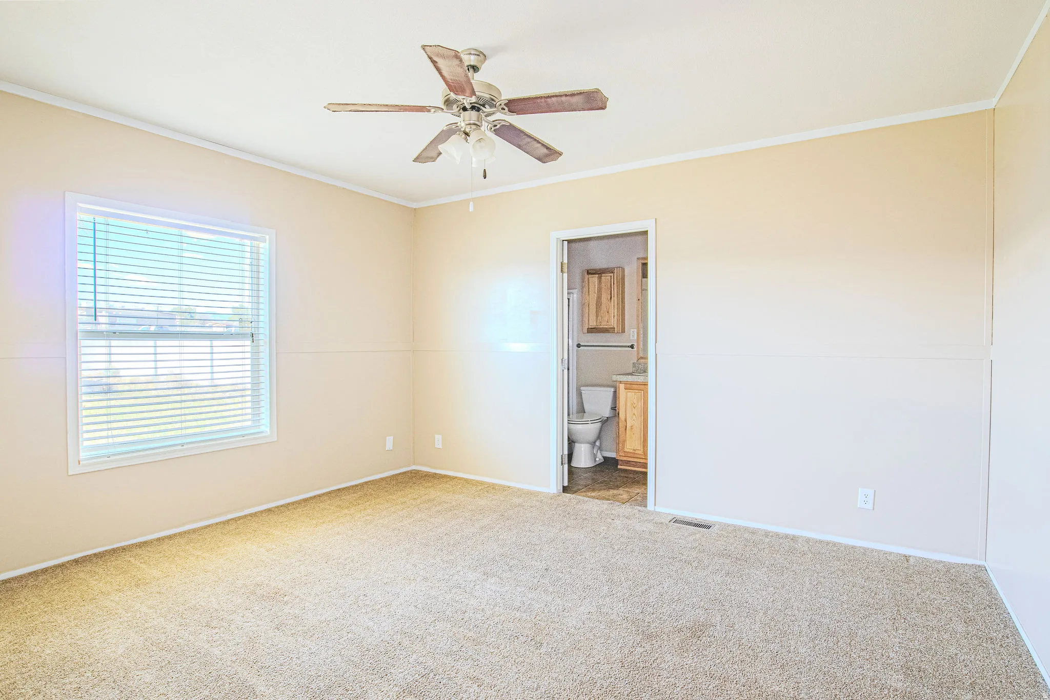 Carpeted room featuring a window with blinds, a ceiling fan, and access to a bathroom with a toilet and vanity