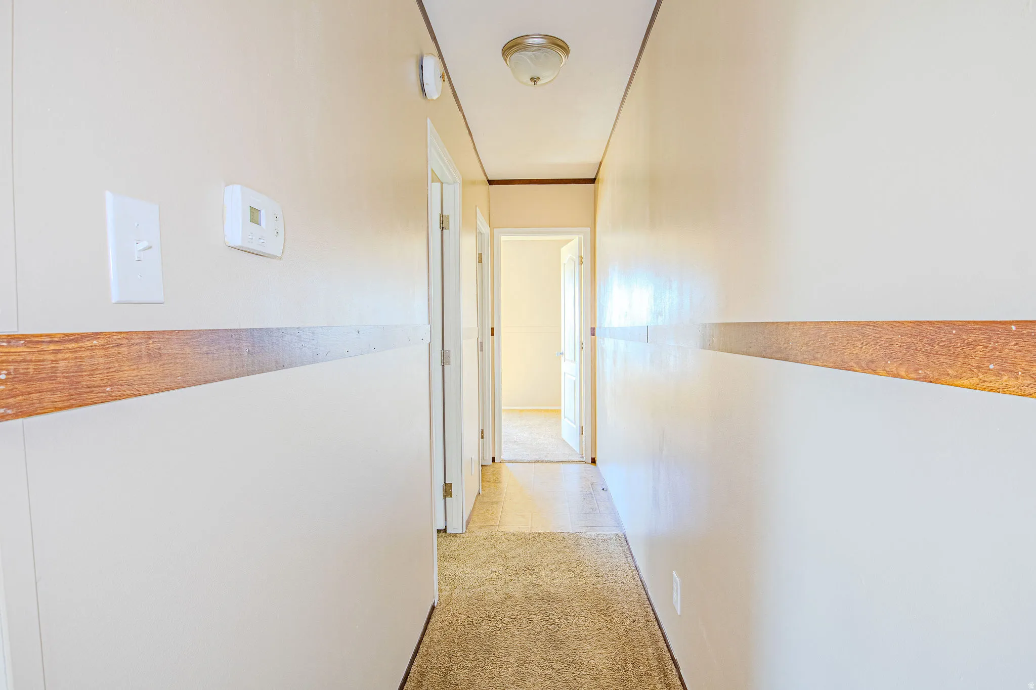 Hallway featuring light-colored walls with a wood-finish accent strip, neutral carpet flooring, and a flush-mount ceiling light fixture