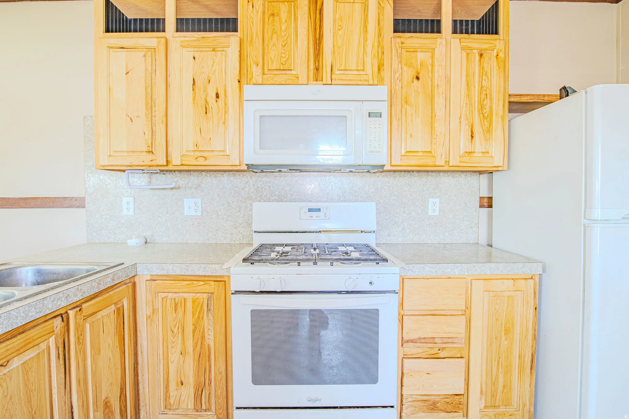 Kitchen featuring natural wood cabinetry, light-toned countertops, a white gas range, an over-range microwave, and a white refrigerator
