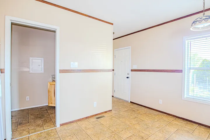 Open interior space featuring light-colored walls with decorative trim, square tile flooring, a window with blinds, and a paneled entry door