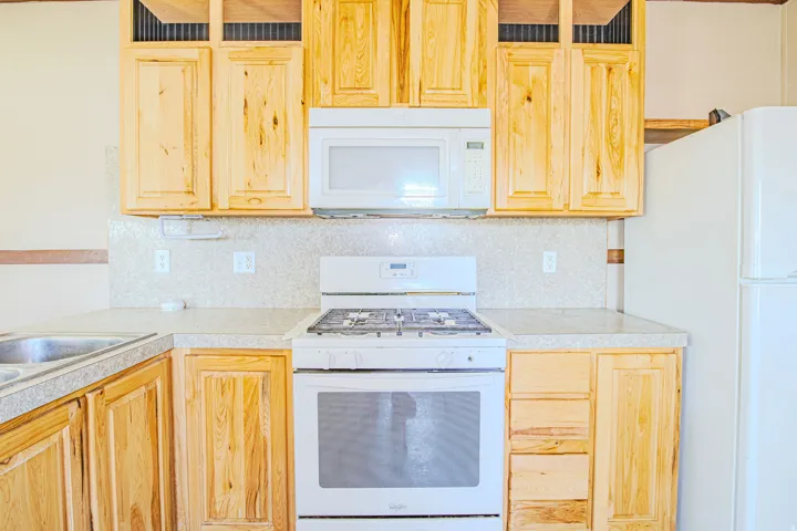 Kitchen featuring natural wood cabinetry, light-toned countertops, a white gas range, an over-range microwave, and a white refrigerator
