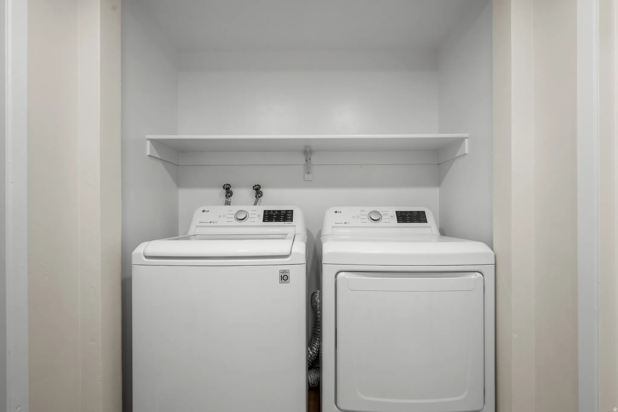 Dedicated laundry area featuring a top-loading washing machine and front-loading dryer, complete with a white overhead shelving unit and visible utility hookups