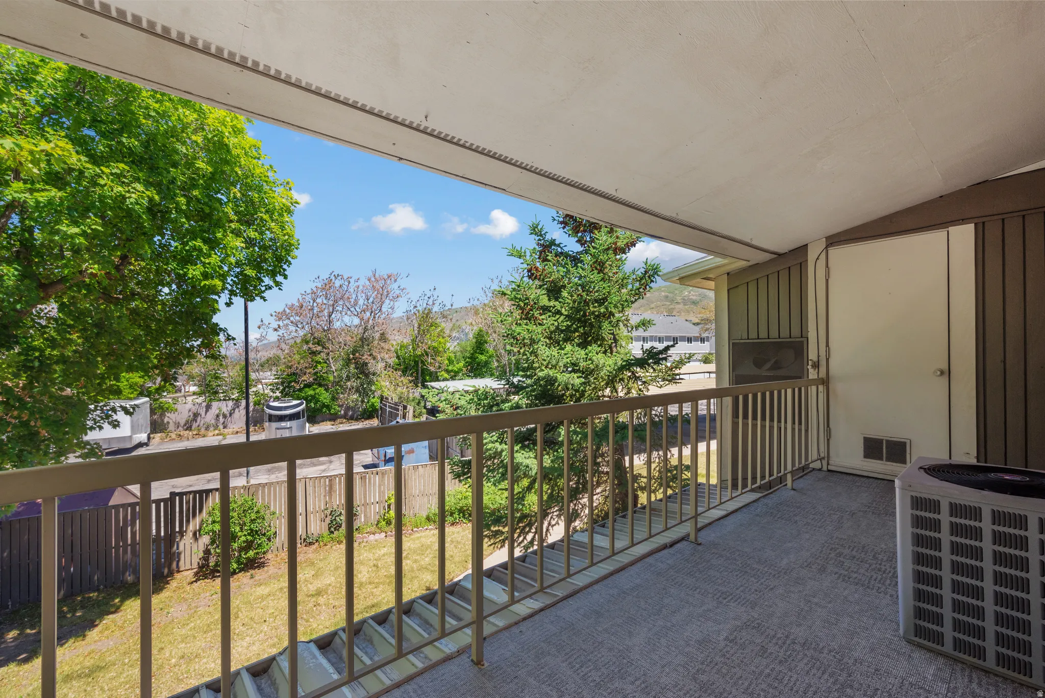Covered outdoor balcony featuring a textured flooring surface, a metal railing, and an exterior storage closet