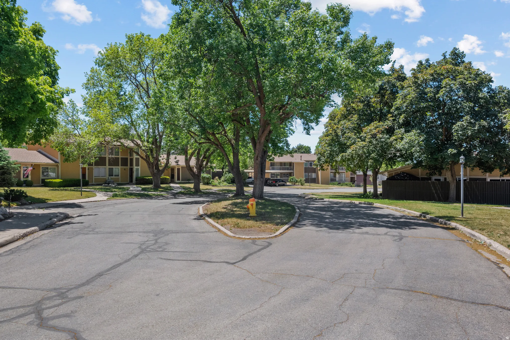 Residential community setting featuring mature trees, paved roadways, and landscaped green spaces