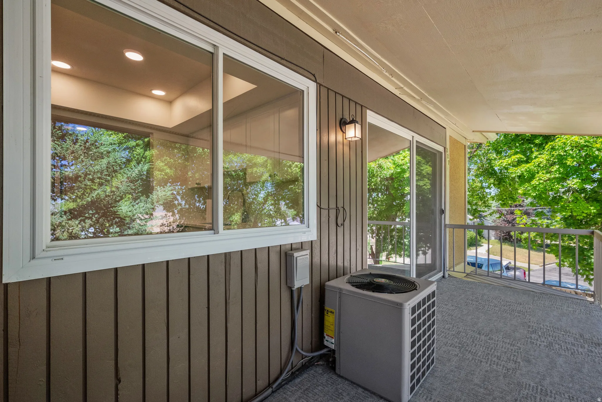 Private outdoor balcony featuring a textured floor, painted railing, and exterior wall light fixture