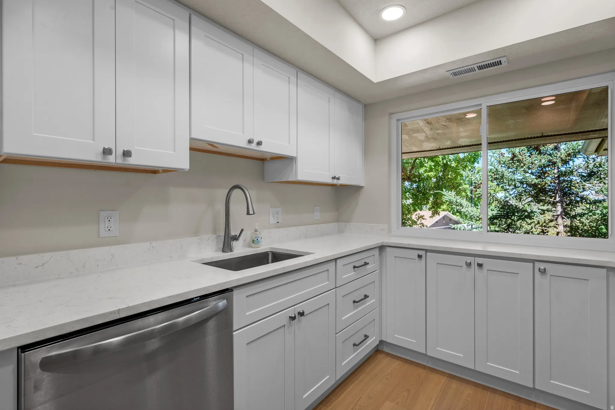 Modern kitchen featuring white shaker cabinetry, light-toned quartz countertops, and a stainless steel sink with a gooseneck faucet