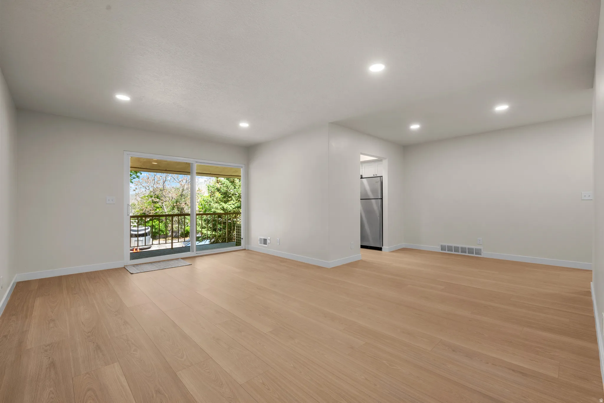 Spacious room featuring light wood-finish flooring, recessed lighting, and a sliding glass door opening to a balcony