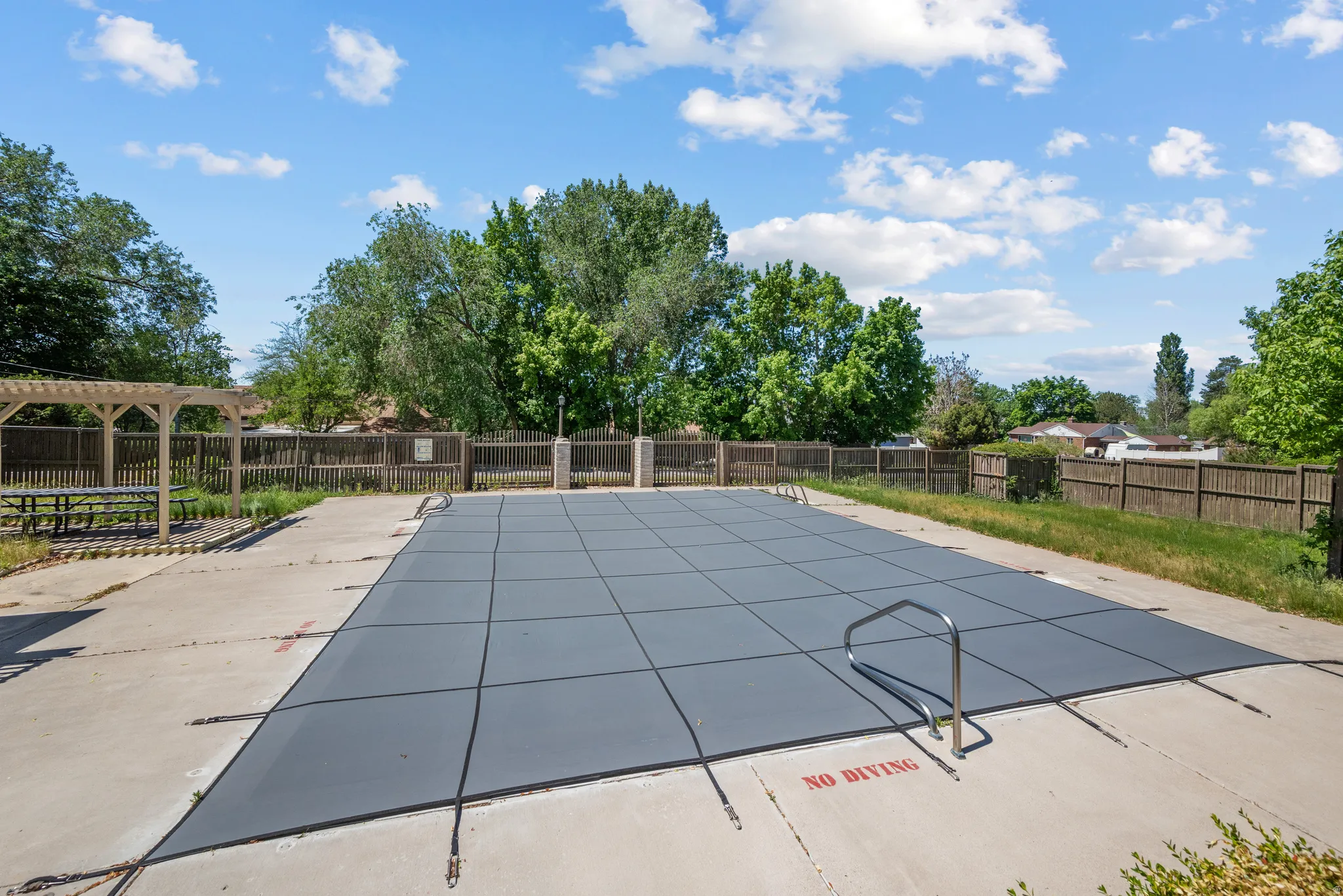 Outdoor swimming pool featuring a dark gray safety cover, concrete surround, and perimeter fencing