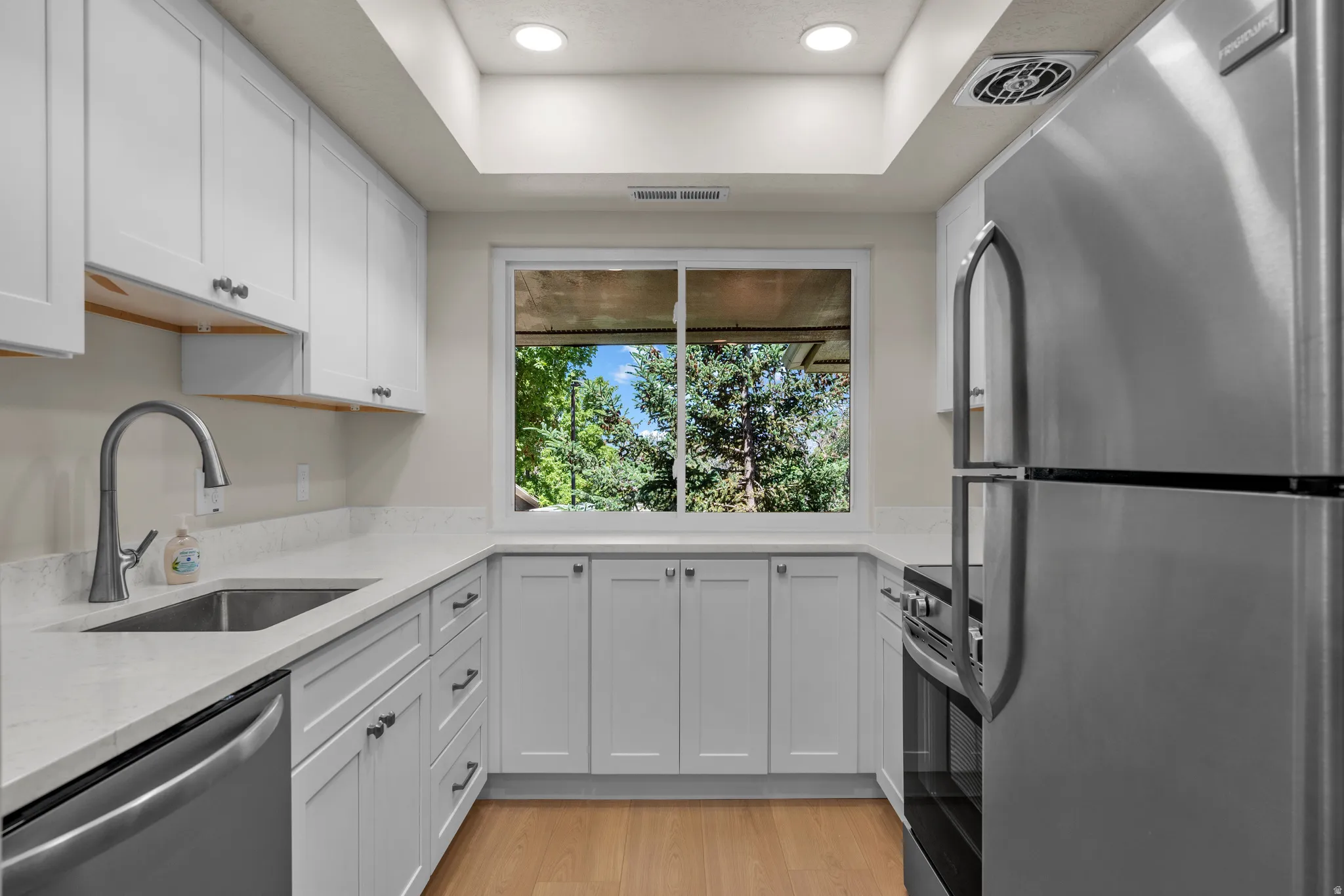 Modern kitchen featuring white shaker cabinetry, light-toned quartz countertops, and stainless steel appliances