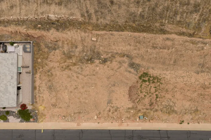 Expansive undeveloped lot presenting a level building area, a paved street frontage, and a partially developed retaining wall at the rear property line