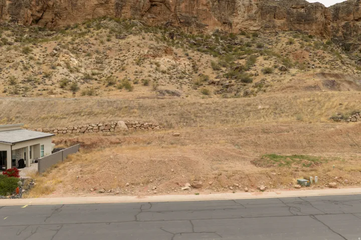 Level building lot featuring a paved roadway frontage, a stone retaining wall, and desert landscaping