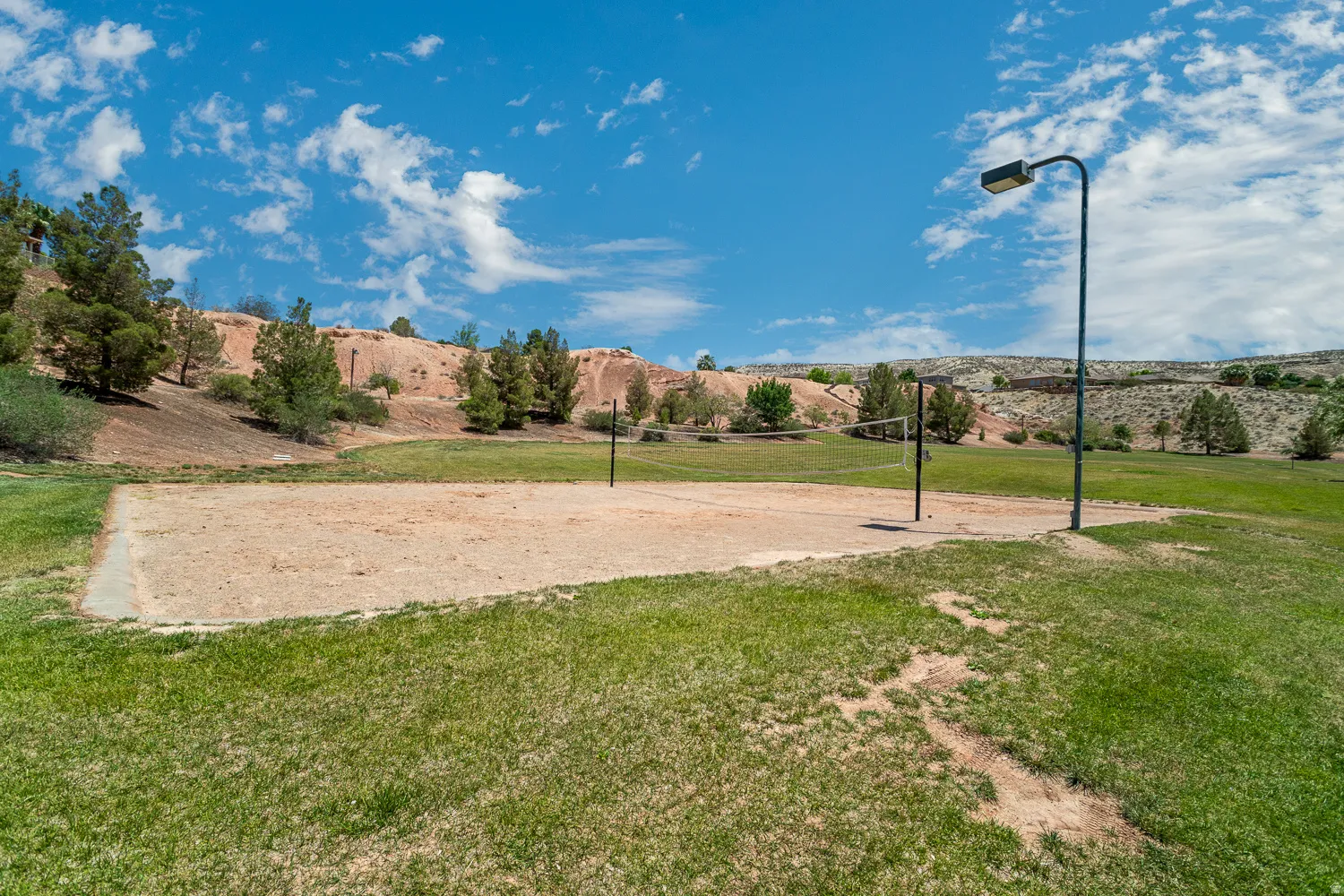 Outdoor sand court with a net, bordered by green grass