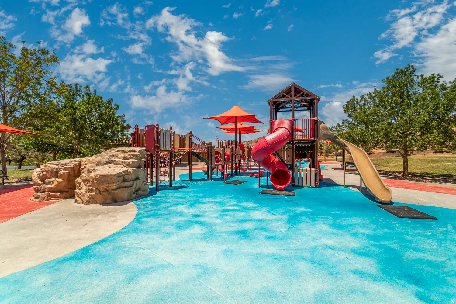 Expansive recreational area featuring a multi-level play structure with slides, rock-climbing elements, and shade canopies