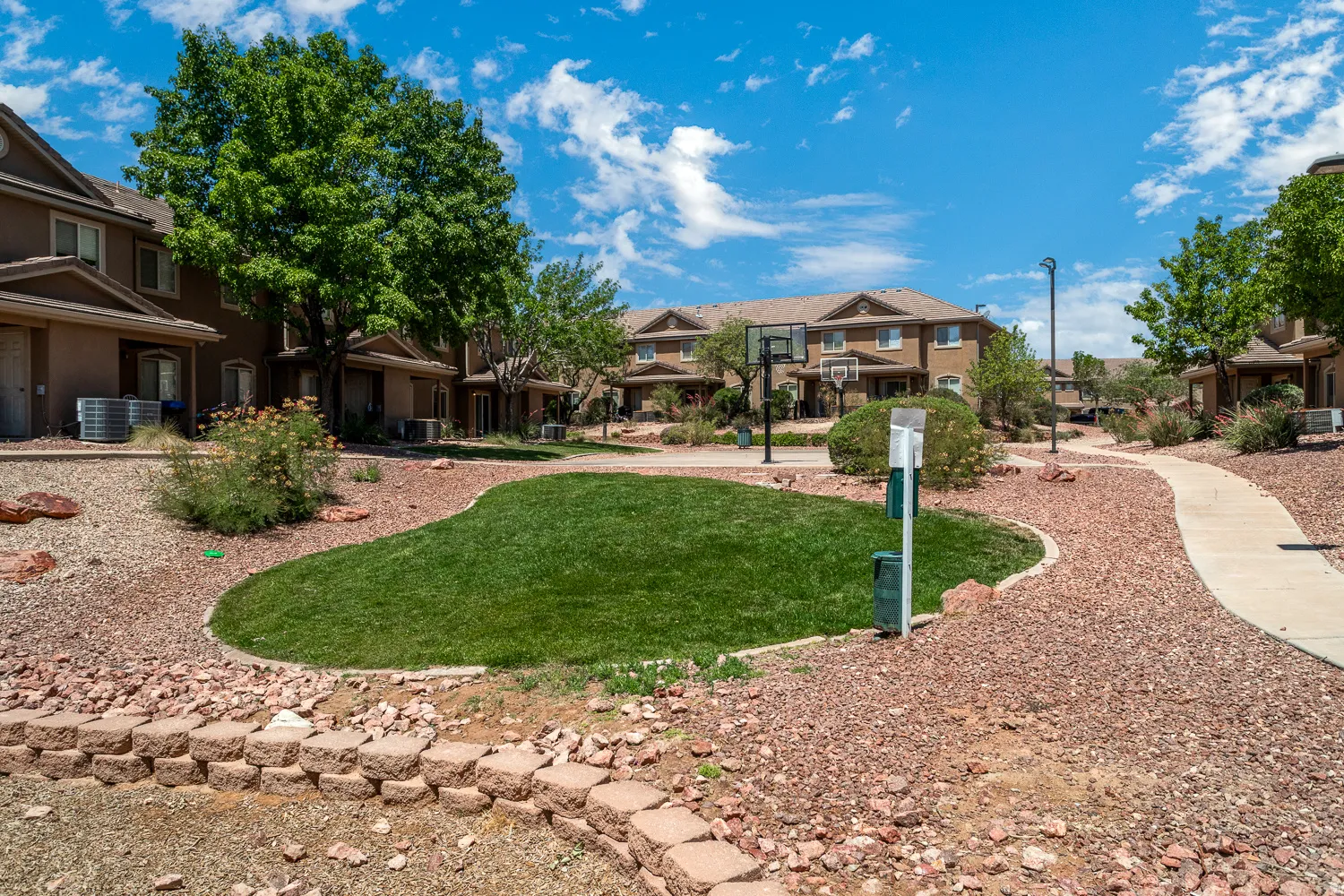 Community green space featuring a manicured lawn, paved walkways, and mature trees