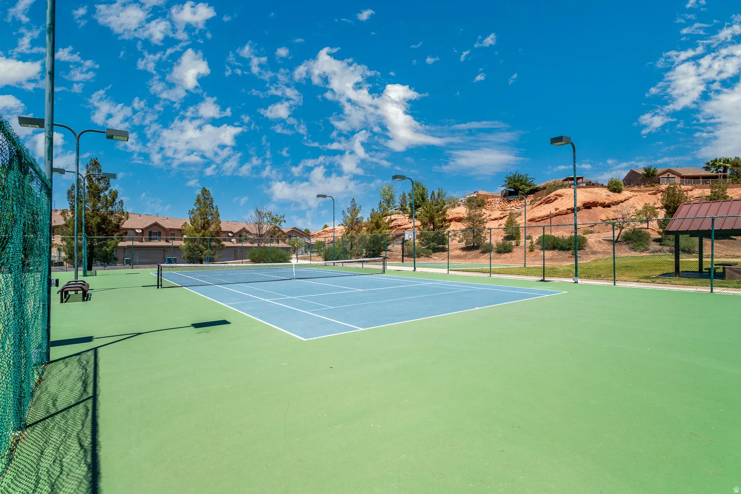 Tennis court with a light blue playing surface and green surrounds