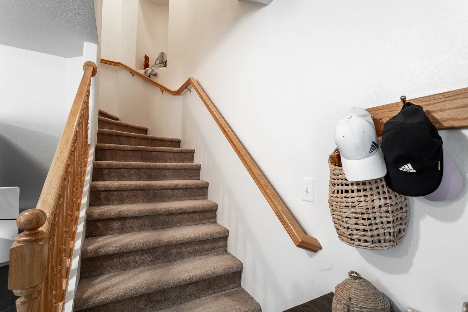 Carpeted staircase featuring a natural wood handrail and matching balusters