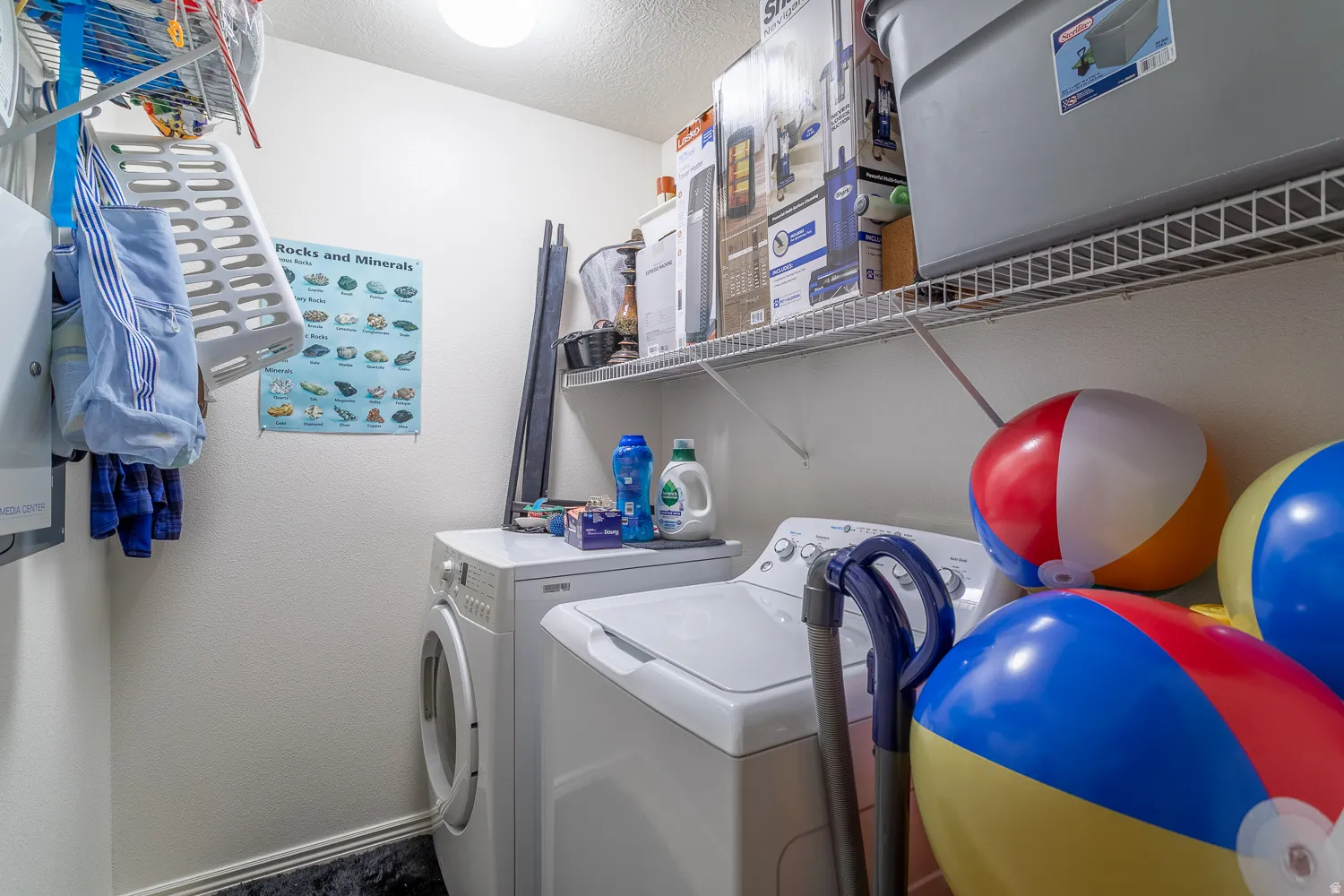 Dedicated laundry area featuring a front-load washer, a top-load dryer, and overhead wire shelving for organized storage