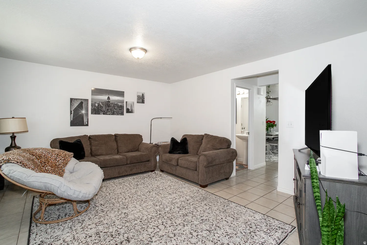 Bright living area featuring light-toned tile flooring, white walls, and a ceiling-mounted light fixture