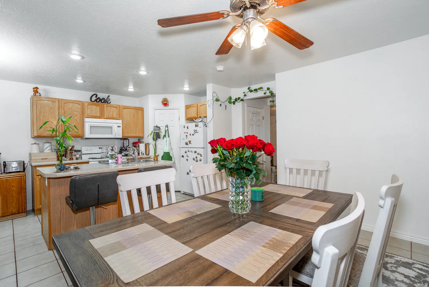 Dining area featuring a wood-finish table, white chairs, and a ceiling fan with light fixture