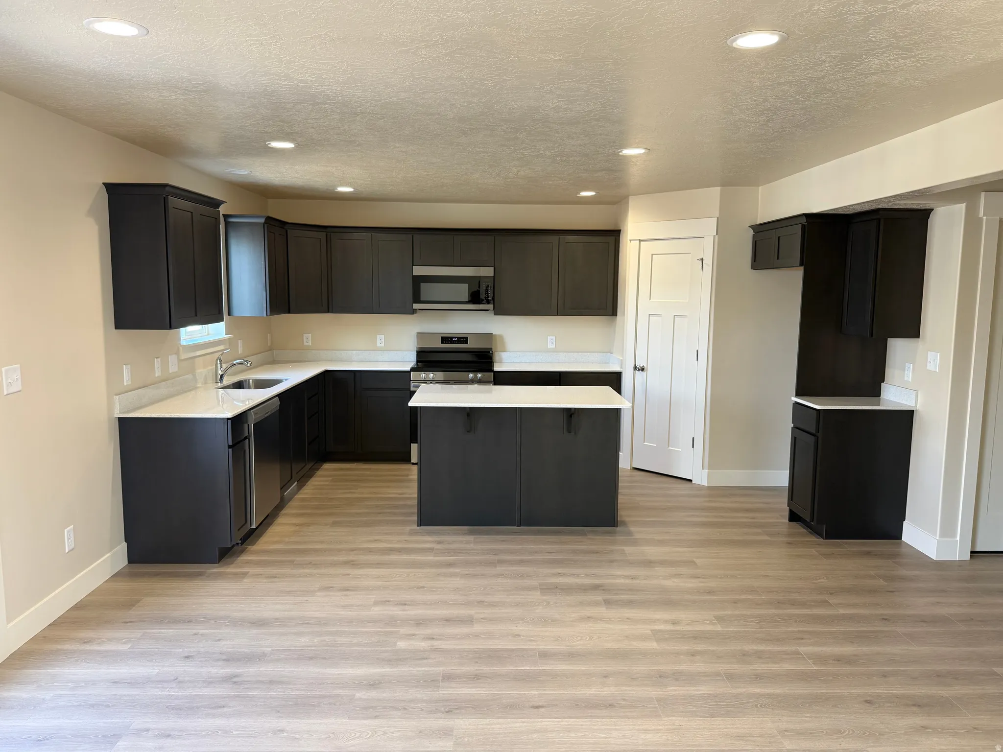 Open-concept kitchen featuring dark wood cabinetry, light-toned countertops, and wood-finish flooring