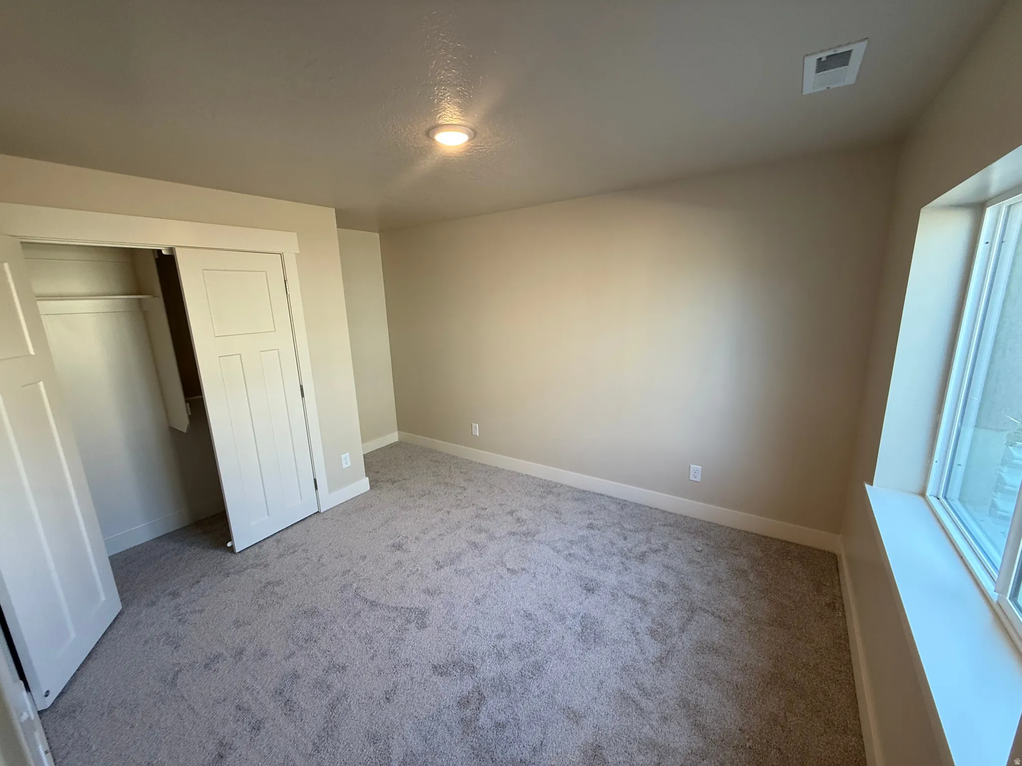 Neutral-toned room featuring a single window, recessed ceiling lighting, and light gray carpeting