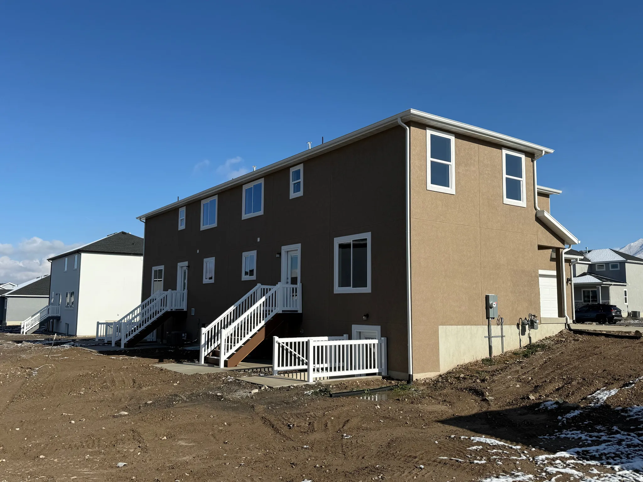 Brown stucco exterior with white trim, multiple rear entry doors, and white railings on exterior staircases