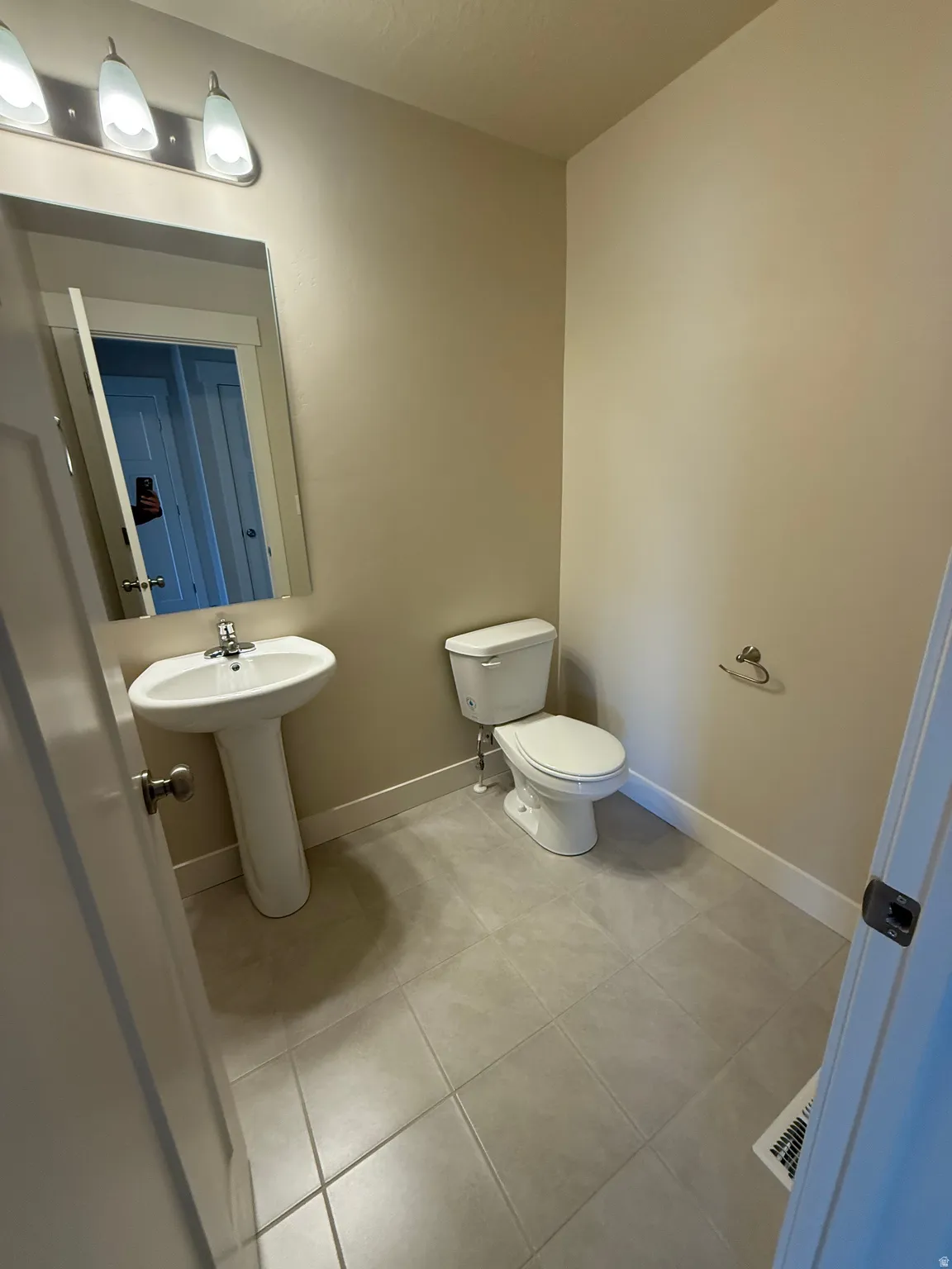 Pedestal sink featuring a chrome faucet, large vanity mirror, three-light fixture, ceramic tile flooring, and a white toilet