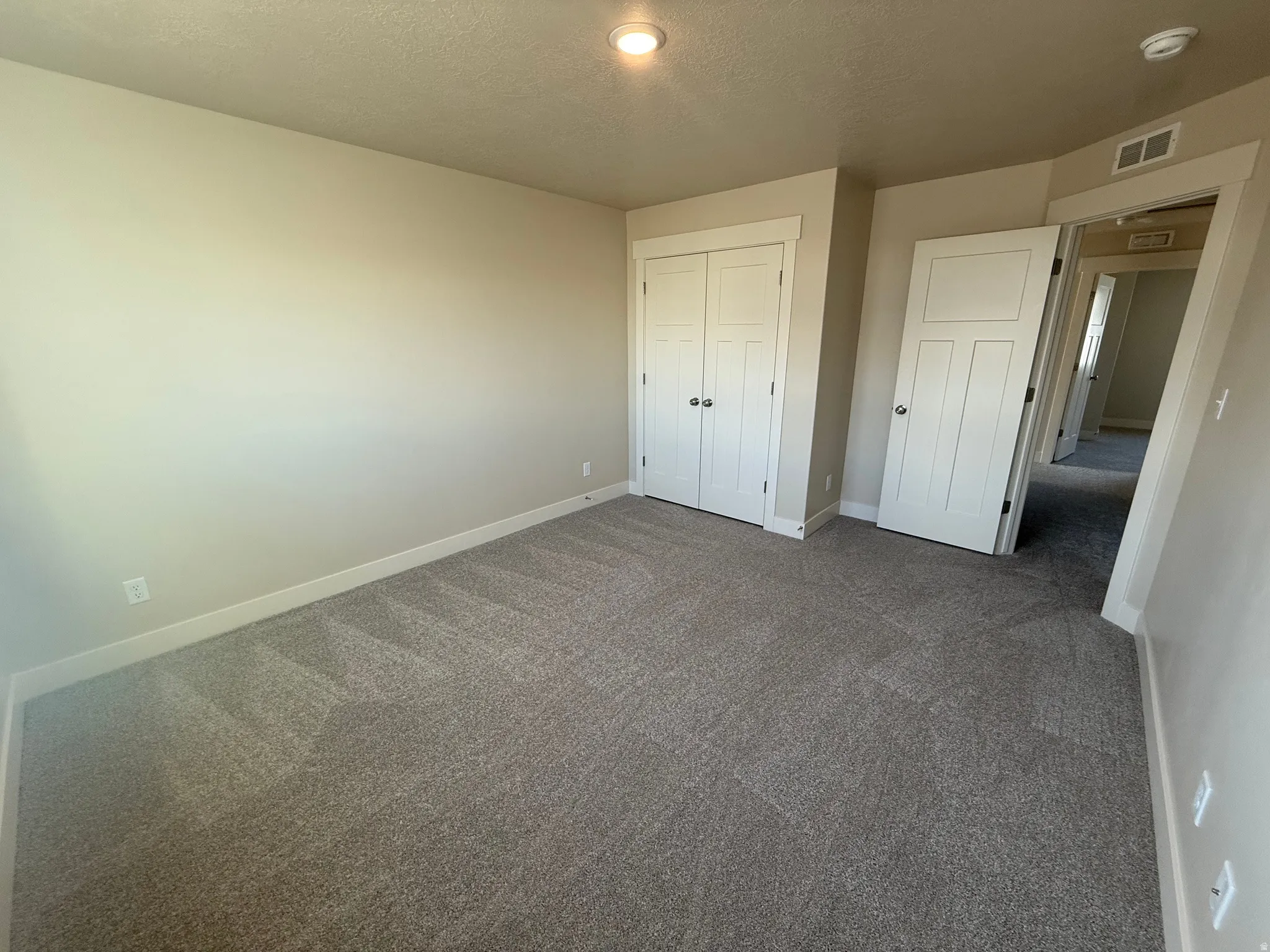 Carpeted room with a neutral wall palette, featuring a double-door closet with white paneled doors, and a standard white paneled door entryway