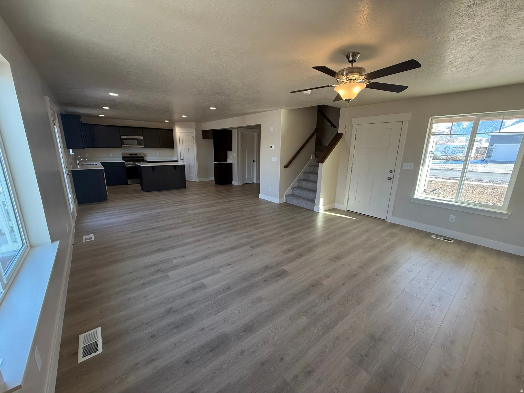 Open-concept living area with wood-finish flooring, recessed lighting, and a contemporary ceiling fan