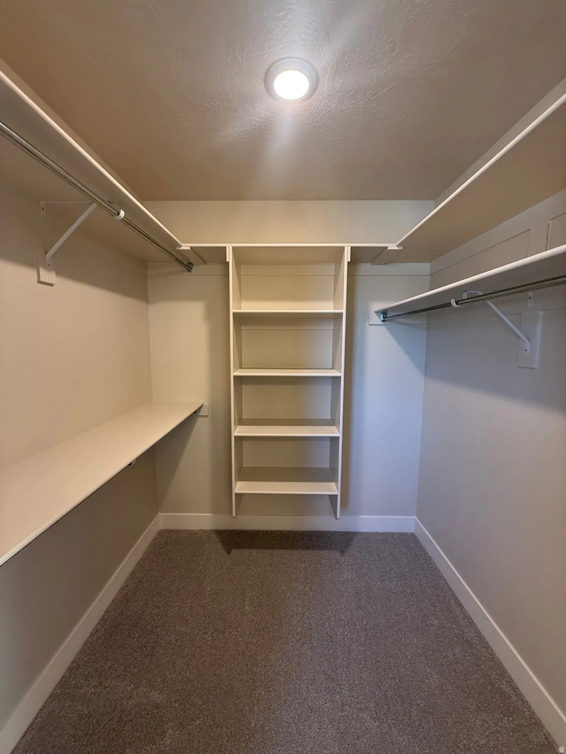 Recessed ceiling lighting illuminates a walk-in closet featuring built-in shelving, multiple hanging rods, and an integrated storage unit