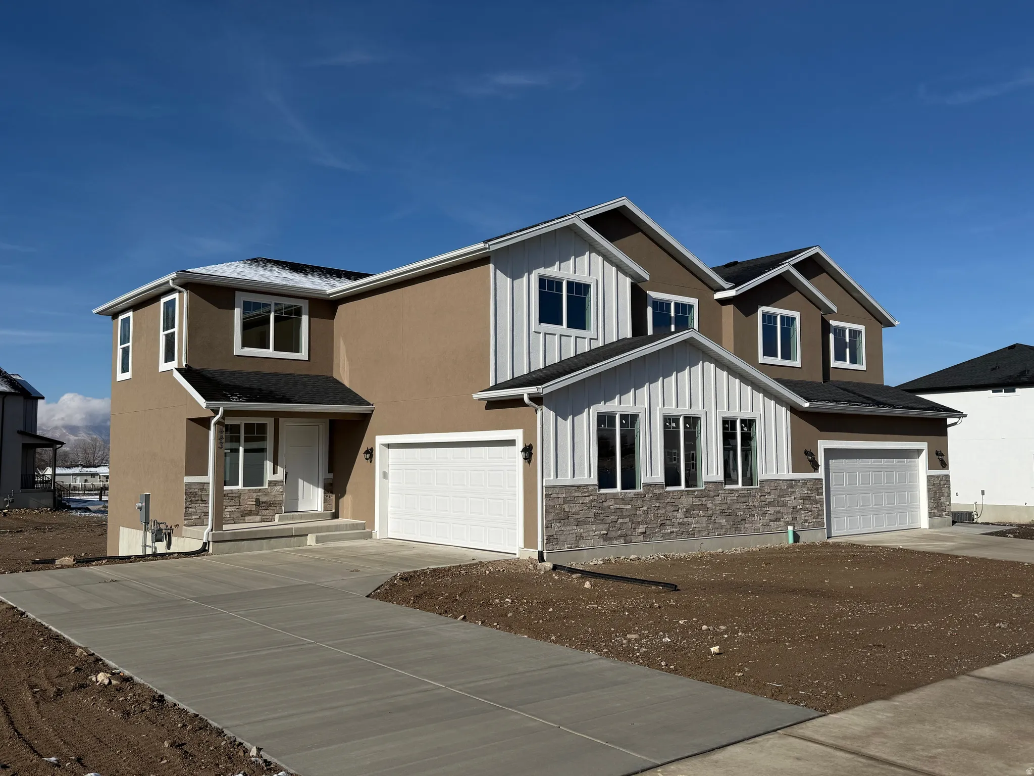 Contemporary two-story exterior featuring a multi-textured facade with stucco, board and batten siding, and stone accents