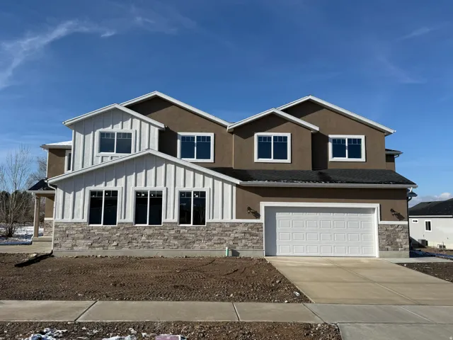 Contemporary two-story residence featuring a two-car garage, mixed exterior finishes of stucco, vertical siding, and stone veneer, and multiple prominent gables