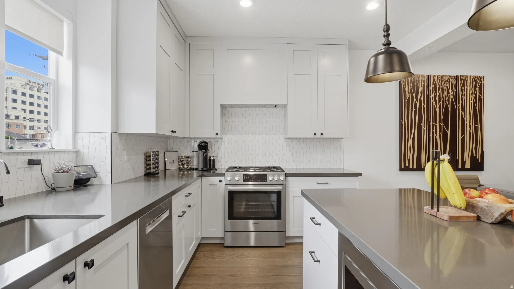 Modern kitchen featuring white shaker cabinetry, stainless steel appliances, a tile backsplash, dark countertops, and wood-finish flooring